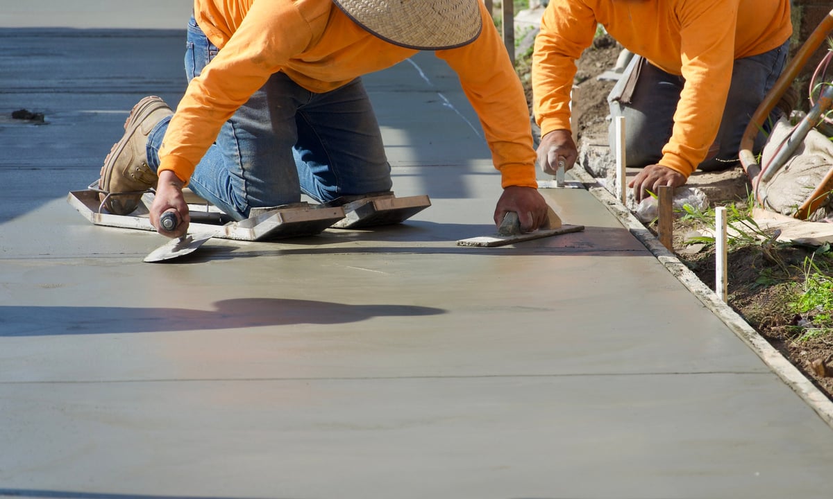 Construction crew pouring and finishing the concrete driveway and sidewalk of a modern duplex development, with a concrete truck nearby
